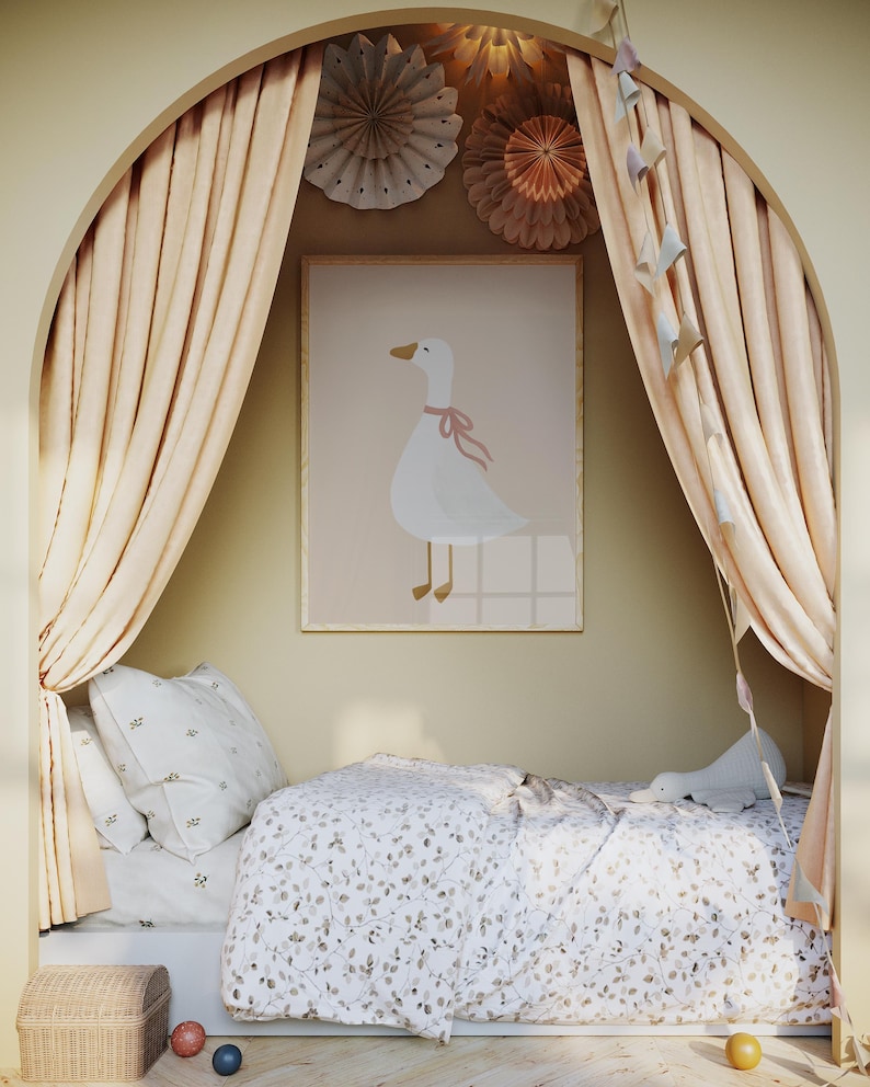May include: A children's bedroom scene featuring a framed print of a white goose with a pink bow. The room has a bed with floral bedding, pillows, and a small wicker chest. Soft peach-colored curtains frame the bed, and decorative paper fans adorn the wall.