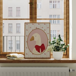 May include: A framed print of a white goose with a red bow tie on a pink background with a pattern of white cherries on a light brown background.