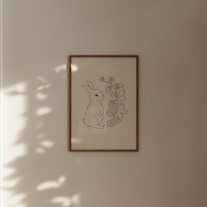 May include: A framed print of a white rabbit standing next to a line drawing of a strawberry plant with pink strawberries.