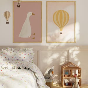 May include: Two framed prints with a pink background. The left print features a white goose sitting on a branch. The right print features a yellow hot air balloon with white stripes.