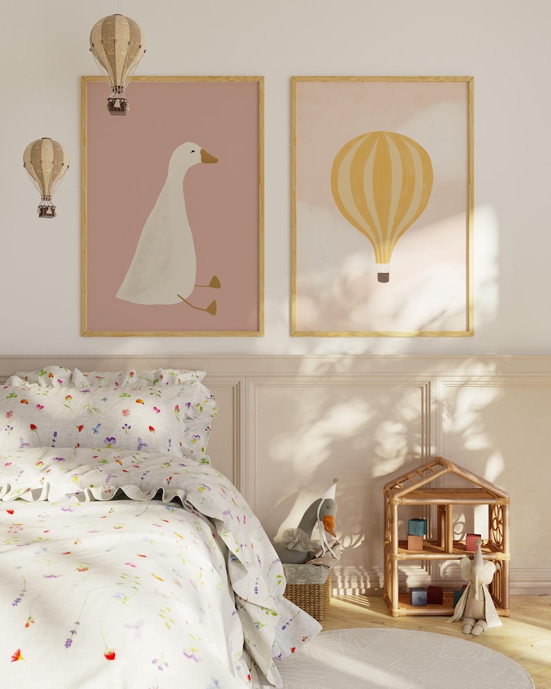 May include: Two framed prints with a pink background. The left print features a white goose sitting on a branch. The right print features a yellow hot air balloon with white stripes.
