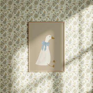 May include: A framed print of a white goose with a light blue bow sitting on a light brown background. The print is surrounded by a thin wooden frame.