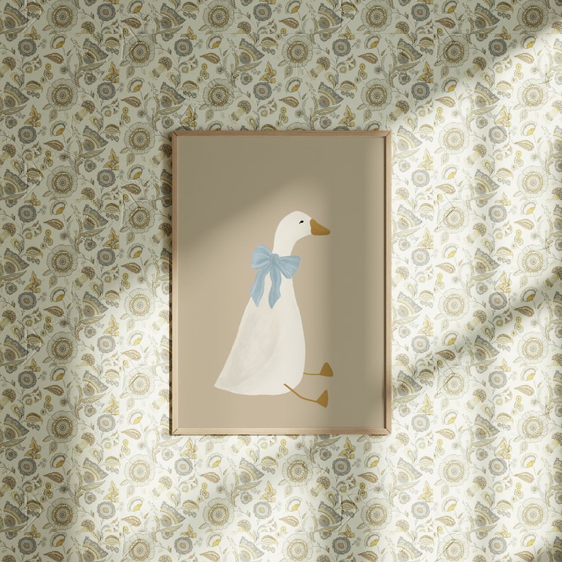May include: A framed print of a white goose with a light blue bow sitting on a light brown background. The print is surrounded by a thin wooden frame.