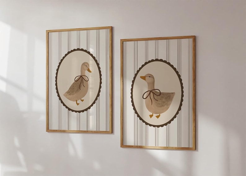 May include: Two framed prints with a striped background and a brown circular border. Each print features a watercolor illustration of a duck with a brown bow.