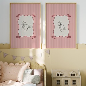 May include: Two framed prints with pink and white striped backgrounds. Each print features a black and white illustration of a duck with a bow on its head, set within a red frame with a decorative border.
