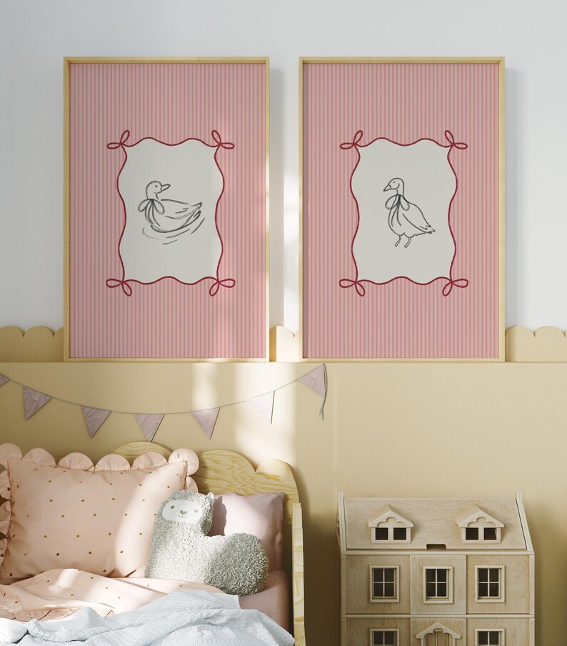 May include: Two framed prints with pink and white striped backgrounds. Each print features a black and white illustration of a duck with a bow on its head, set within a red frame with a decorative border.