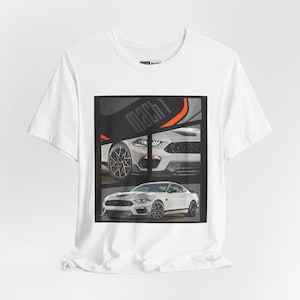 May include: White t-shirt featuring a graphic print of a white Ford Mustang Mach 1. The car is shown in two different angles, with the text "Mach 1" printed on the side of the car.