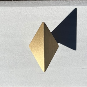 May include: A gold diamond-shaped cabinet knob with a brushed finish.