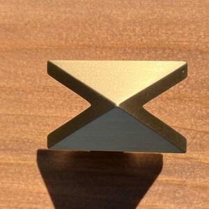 May include: A gold-toned metal cabinet knob with a geometric, pyramid-shaped design.