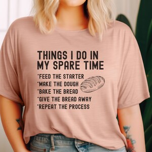 May include: A pink t-shirt with the text "THINGS I DO IN MY SPARE TIME" and a list of activities related to baking bread: *FEED THE STARTER *MAKE THE DOUGH *BAKE THE BREAD *GIVE THE BREAD AWAY *REPEAT THE PROCESS. A drawing of a loaf of bread is next to the list.