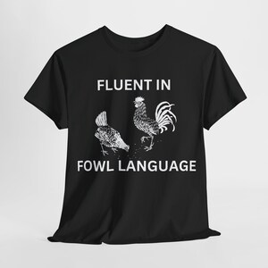 Puede incluir: Camiseta negra con un gráfico blanco de un gallo y una gallina. El texto "Fluent in Fowl Language" está impreso debajo del gráfico.