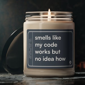 Può includere: Una candela di cera di soia in un barattolo di vetro trasparente con un'etichetta nera che recita "smells like my code works but no idea how".