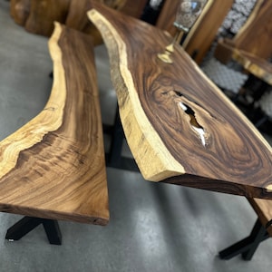 May include: A live edge wood table and bench set with black metal legs. The table and bench are made of dark brown wood with a natural live edge finish.