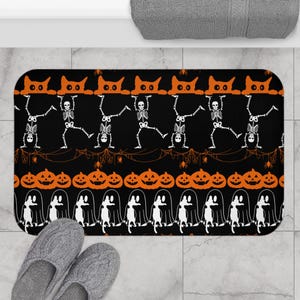 Op de afbeelding: Een rechthoekige badmat met een zwarte achtergrond en een herhalend Halloween-patroon. Het ontwerp bevat oranje kattensilhouetten, witte skeletten in verschillende houdingen, oranje pompoenen en witte spookomtrekken met spinnen.