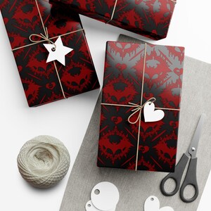 May include: Three wrapped gifts with red and black bat-themed wrapping paper, tied with twine and white tags. A ball of twine, scissors, and blank tags are also present, suggesting a DIY gift-wrapping theme.