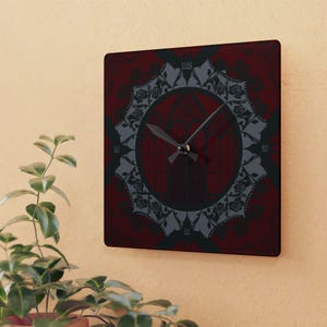 May include: A square wall clock featuring a deep red background with a dark, intricate circular pattern of roses and gothic-style arches. The clock face includes black hour and minute hands, with the numbers 3, 6, 9, and 12 displayed in a simple font.