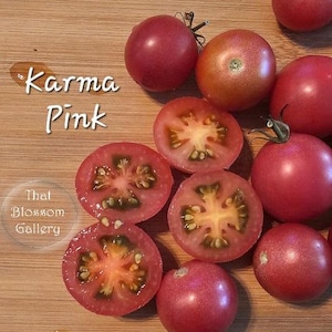 May include: A close-up of a group of pink tomatoes, some whole and some cut in half, on a wooden surface. The tomatoes are labeled "Karma Pink".