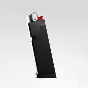 May include: A black lighter with a red ignition button and a silver metal top. The lighter is angled slightly to the left against a white background. The lighter is a rectangular shape.