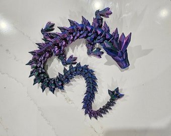 May include: A 3D printed dragon figurine with a purple and green iridescent finish. The dragon is curled up with its tail wrapped around its body.