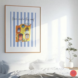 May include: A framed art print with a watercolour illustration of a vibrant house, the text reads "Love, under this roof." The house is set against blue and white vertical stripes. The artwork is displayed above a bed with white linens.