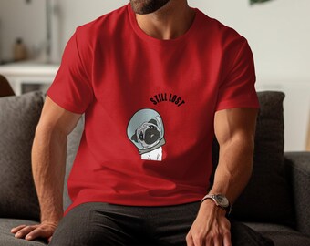 May include: Red t-shirt featuring a cartoon pug wearing a space helmet. The text "STILL LOST" is above the pug. The shirt is a solid red color.