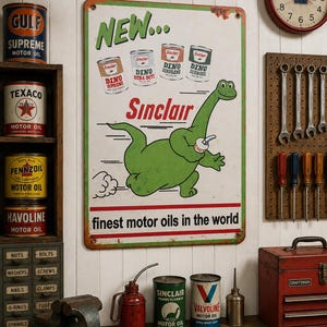 May include: A rectangular metal sign featuring a green cartoon dinosaur holding a cup, with the text "NEW...", "Sinclair", and "finest motor oils in the world". The sign displays four small motor oil cans at the top and has a green border.