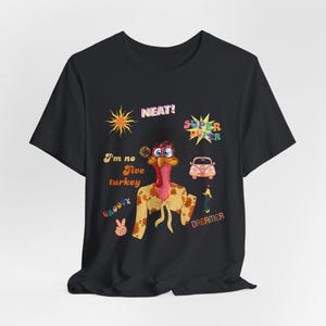 Puede incluir: Camiseta negra con un gráfico colorido de un pavo que lleva gafas de sol y una corona de flores. El gráfico incluye el texto "I'm no five turkey", "Neat!", "Super Duper", "Groovy" y "Dreamer".
