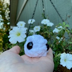 Puede incluir: Un pequeño juguete de peluche blanco con ojos negros. El juguete tiene forma de bola redonda con una superficie texturizada.