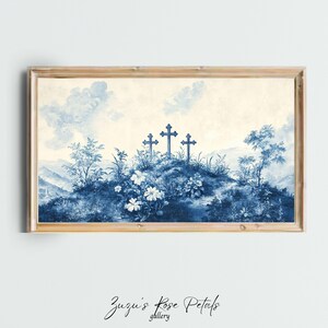May include: A framed blue and white print of a landscape with three crosses on a hill. The print is in a light wood frame.