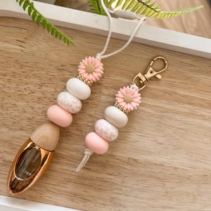 May include: A pink and white beaded keychain with a gold charm and a small glass bottle diffuser. The beads are decorated with a floral pattern and a leopard print.