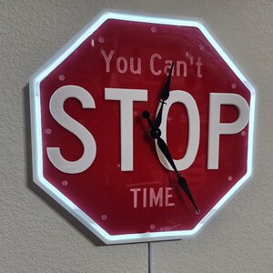 May include: A red stop sign shaped clock with white lettering that reads "You Can't Stop Time". The clock hands are black and the background is red.