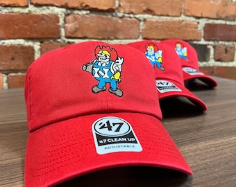 May include: Three red baseball caps with an embroidered cartoon character wearing a blue jumpsuit and holding a wrench. The character is on fire. The caps have a white logo with the number 47 and the text "47 CLEAN UP ADJUSTABLE".