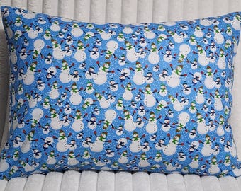 May include: A rectangular pillow featuring a repeating pattern of white snowmen on a bright blue background. Each snowman wears a colorful hat and scarf, with orange carrot noses and black coal buttons, scattered across the fabric surface.