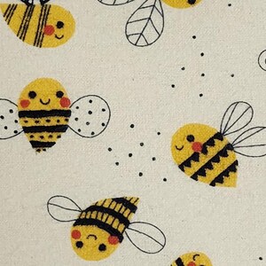 May include: A repeating pattern of cartoon bees on a cream-colored background. The bees are yellow with black stripes, dotted wings, and smiling faces. Small black dots are scattered around the bees.