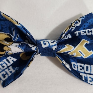 May include: A blue and gold bow tie featuring the words "GEORGIA TECH" and a cartoon yellow jacket mascot. The bow tie has a repeating pattern of the school's name and logo.