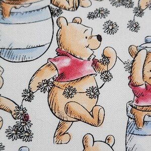May include: A repeating pattern featuring Winnie the Pooh characters in various poses. The illustrations are in a cartoon style, with Pooh wearing a red shirt and surrounded by daisies. The background is white.