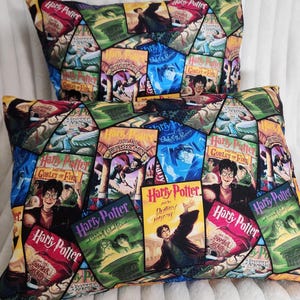 以下が含まれることがあります： ハリーポッターの書籍カバーのパッチワークデザインが施された、2つの長方形の装飾用枕。カバーは赤、青、緑、黄色など様々な色があります。枕は柔らかく、質感のある外観をしています。