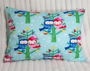 May include: A rectangular pillow featuring a light blue background with a repeating pattern of green Christmas trees, white snowflakes, and pairs of birds wearing colorful winter hats and scarves, decorated with small red and yellow ornaments.
