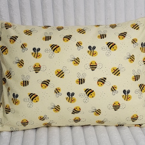 May include: Rectangular pillow with a cream-colored background and a repeating pattern of cartoon bees. The bees are yellow and black with black outlines, and have smiling faces. The pillow is a decorative item.