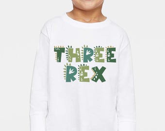 May include: White long-sleeve shirt with a green and brown dinosaur-themed graphic that says "THREE REX".