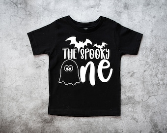 Peut inclure: T-shirt noir avec un fantôme blanc et des chauves-souris. Le texte "The Spooky One" est imprimé sur le t-shirt.