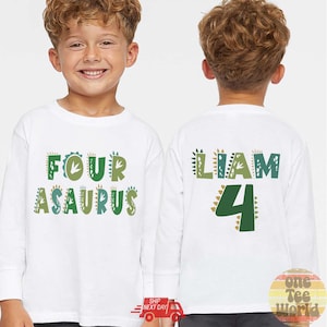 May include: White long-sleeve shirt with the text "FOUR ASAURUS" in green and blue. The back of the shirt has the name "LIAM" and the number "4" in green and gold. A birthday-themed shirt.