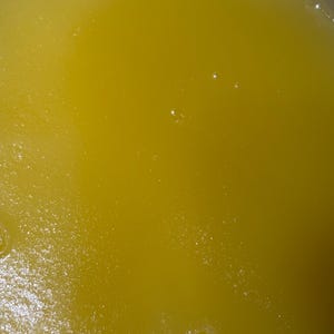 May include: Close-up of a yellow liquid with a slightly textured surface. Small bubbles are visible throughout the liquid, adding a subtle visual texture. The colour is a vibrant, sunny yellow.