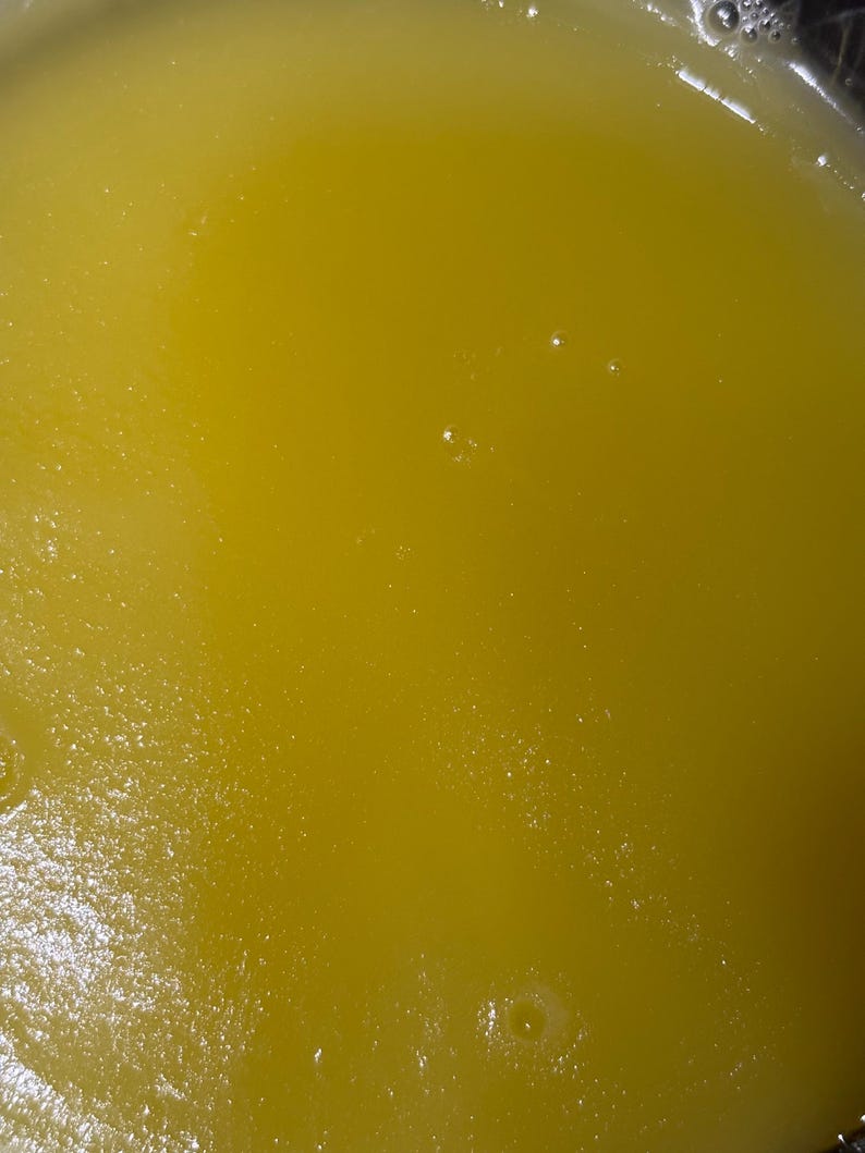 May include: Close-up of a yellow liquid with a slightly textured surface. Small bubbles are visible throughout the liquid, adding a subtle visual texture. The colour is a vibrant, sunny yellow.