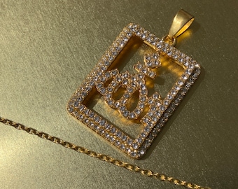 May include: A gold pendant necklace with a square-shaped charm. The charm is covered in clear rhinestones and features a stylized letter 'G' inside.