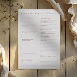 Image of a completed meal planner, sitting on a weathered wooden table. Nearby is dainty yellow flowers in a vase and a linen cloth. Light streams across the paper.