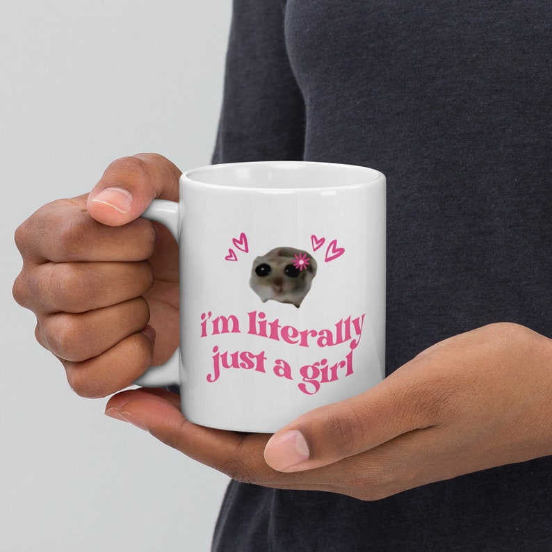Pu&ograve; includere: Tazza in ceramica bianca con un viso di animale rosa in stile cartone animato e il testo "i'm literally just a girl" in lettere rosa.