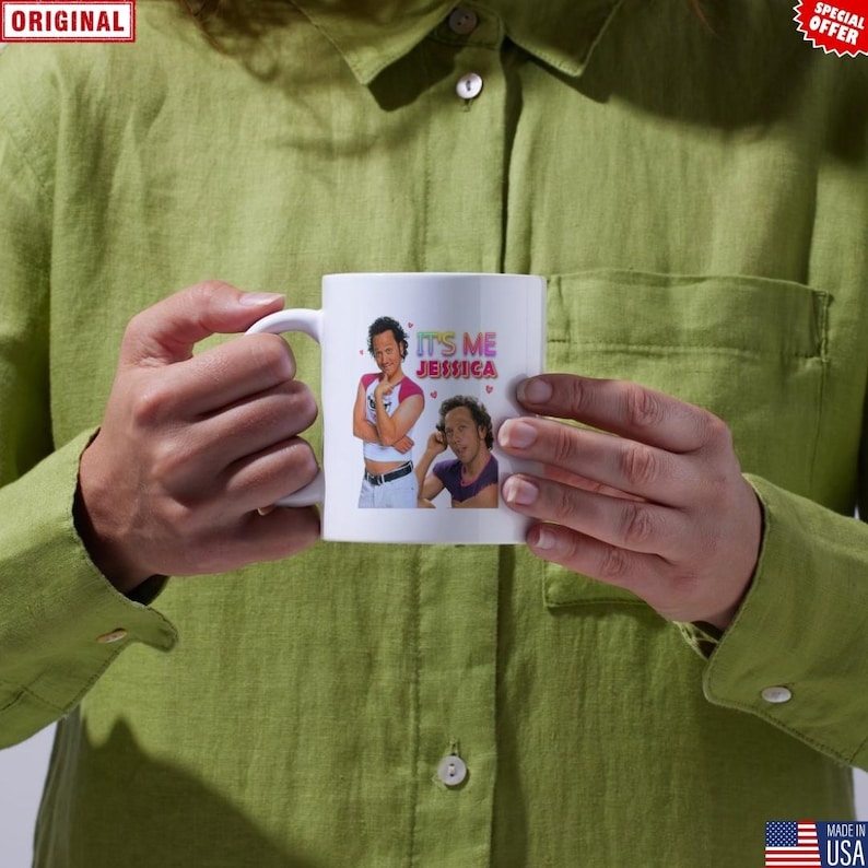 May include: White ceramic mug featuring two images of a person and the text "IT'S ME JESSICA" in pink and purple. The mug is held by a person wearing a green shirt.
