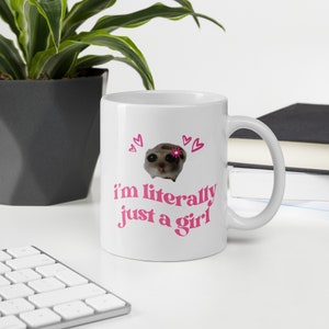 Pu&ograve; includere: Tazza in ceramica bianca con un design rosa. Il design presenta un animale dei cartoni animati con un fiore sulla testa e il testo "i'm literally just a girl".
