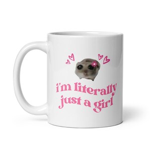 Pu&ograve; includere: Tazza in ceramica bianca con un design a forma di cuore rosa e il testo "i'm literally just a girl" in rosa. Un piccolo animale con un fiore rosa sulla testa &egrave; al centro della tazza.